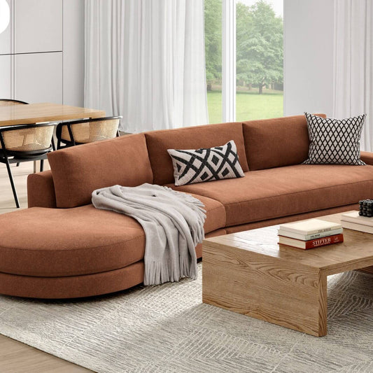 Modern rust-colored sectional sofa with geometric pillows, light oak coffee table, gray rug in bright living room