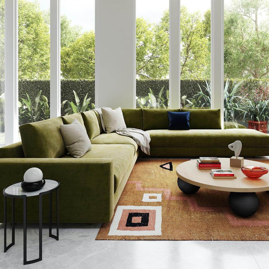 Modern living room with olive green sectional, geometric rug, floor-to-ceiling windows & tropical plants outside