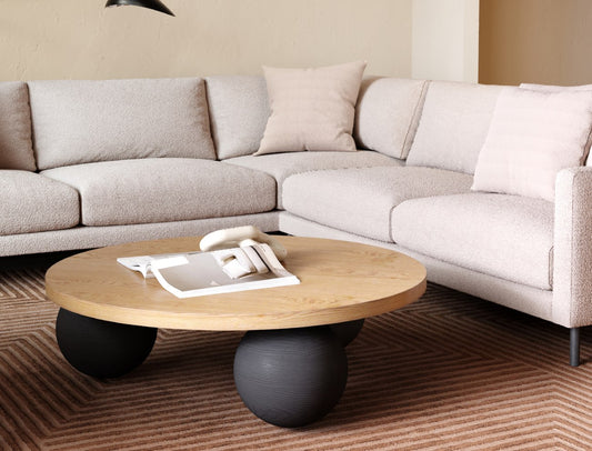 Modern living room with beige sectional sofa, round wooden coffee table with sphere bases, and striped carpet