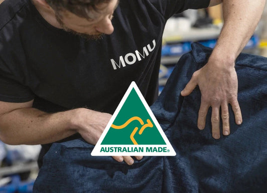 Person wearing MOMU shirt displaying Australian Made logo while working with dark blue fabric material
