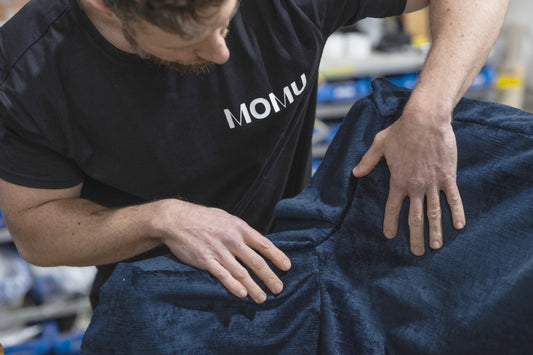 Person in MOMU shirt inspecting dark fabric texture with hands, close-up workshop shot