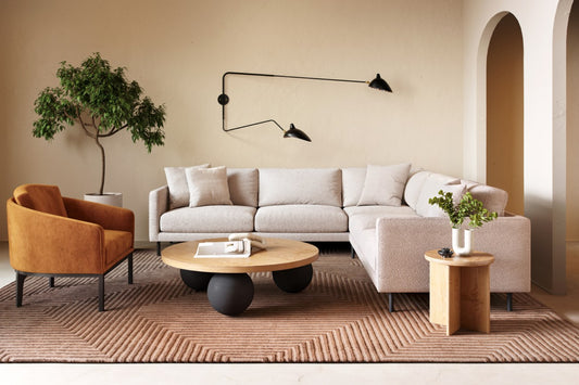 Modern living room with beige sectional, cognac accent chair, geometric rug, and sculptural coffee table.
