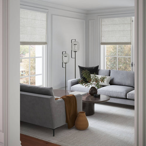 Modern living room with gray sofas, floor lamp, round coffee table, beige Roman shades and brown accents