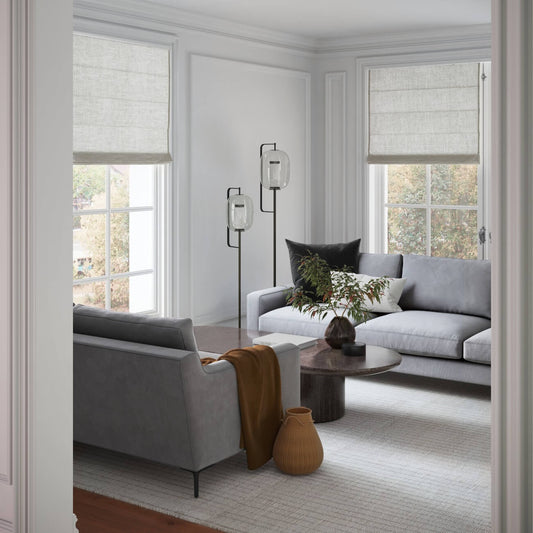 Modern living room with gray sofas, floor lamp, linen window shades, and terracotta accents on neutral carpet