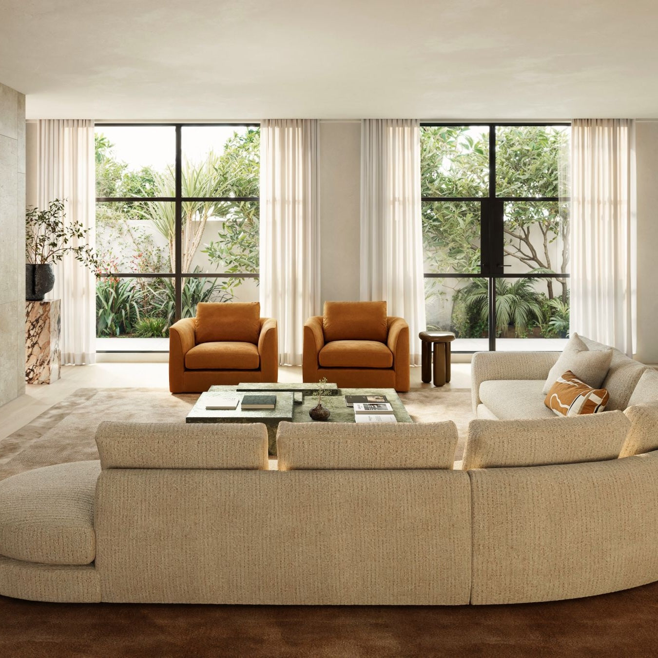 Modern living room with burnt orange armchairs, stone coffee table, and bright window view