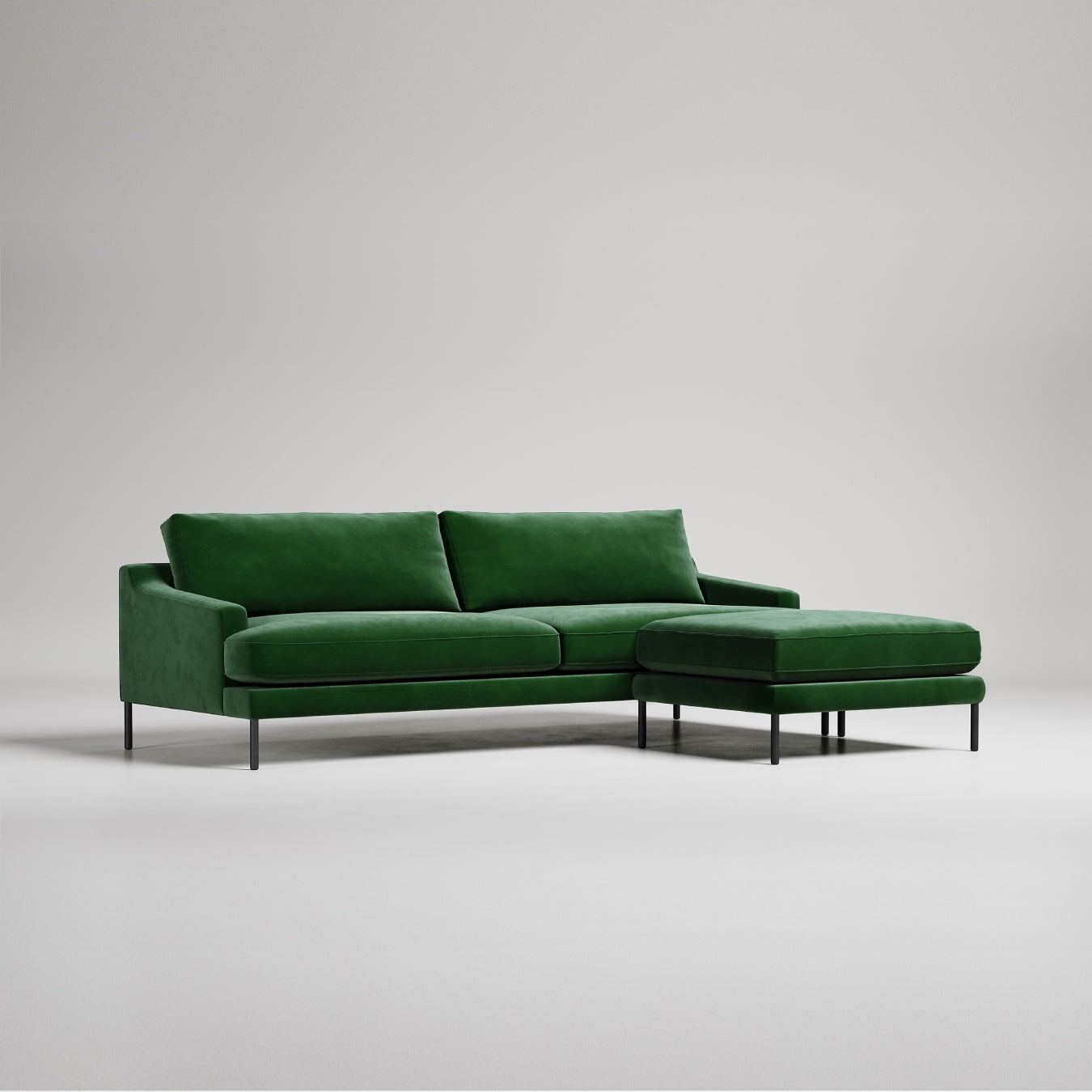 Modern emerald green velvet sectional sofa with ottoman on metal legs against light gray background