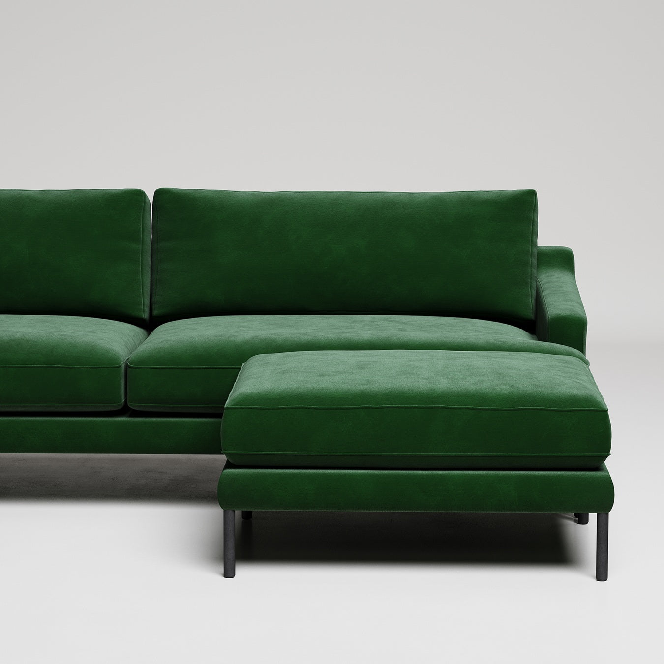 Modern emerald green velvet sectional sofa with matching ottoman on black metal legs against white background