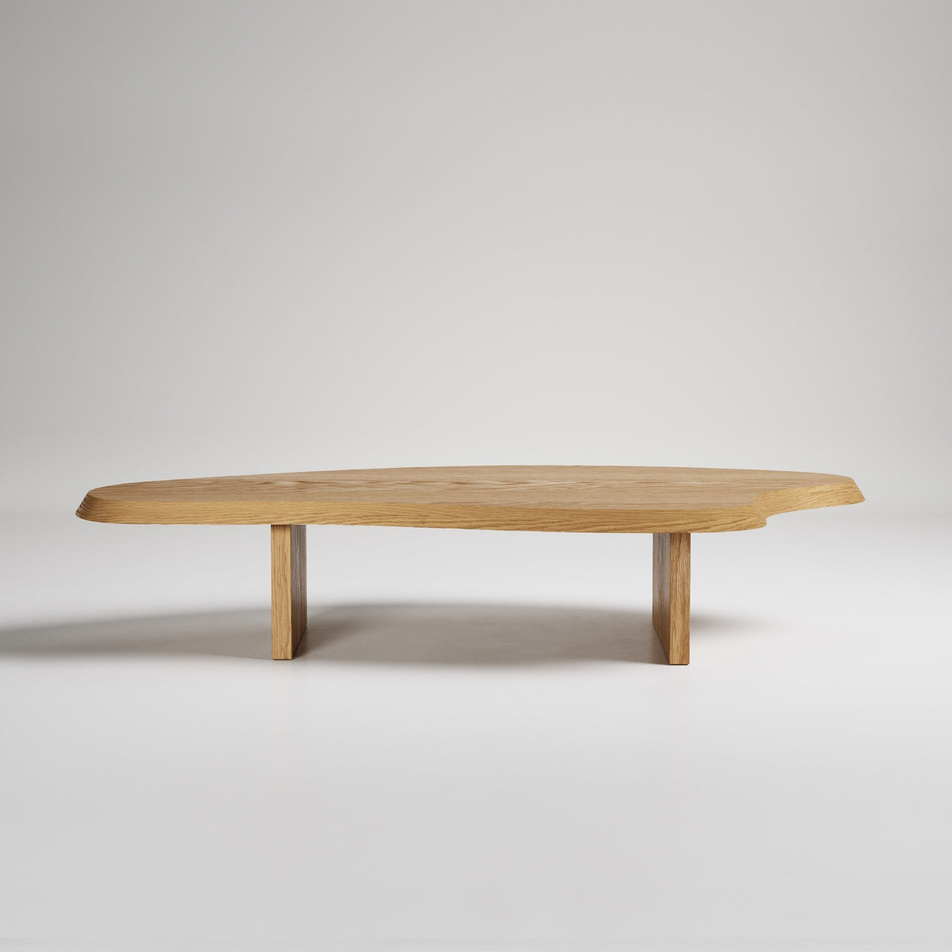 Modern low oak coffee table with organic-shaped top and minimalist rectangular legs against white background