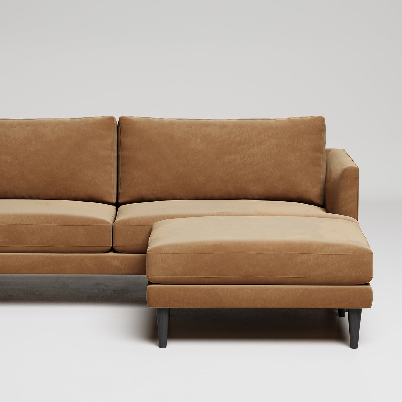 Modern tan leather sectional sofa with chaise lounge on dark legs, against white background