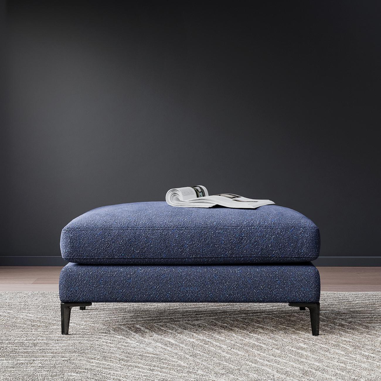 Blue upholstered ottoman with metal legs on gray carpet, open magazine on top, modern minimalist style