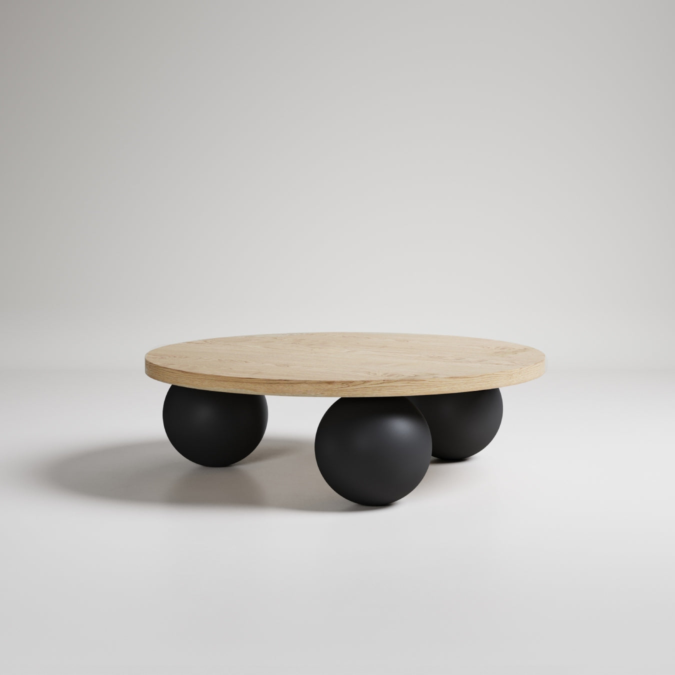 Modern round wood coffee table with three black sphere legs, minimalist design on white background