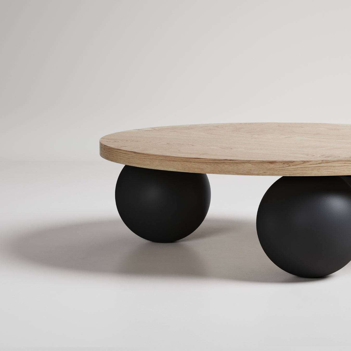 Modern round coffee table with light oak top and matte black sphere legs on white background