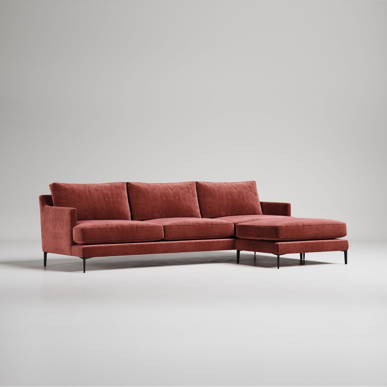 Modern L-shaped sectional sofa in rust velvet upholstery with black metal legs against gray background