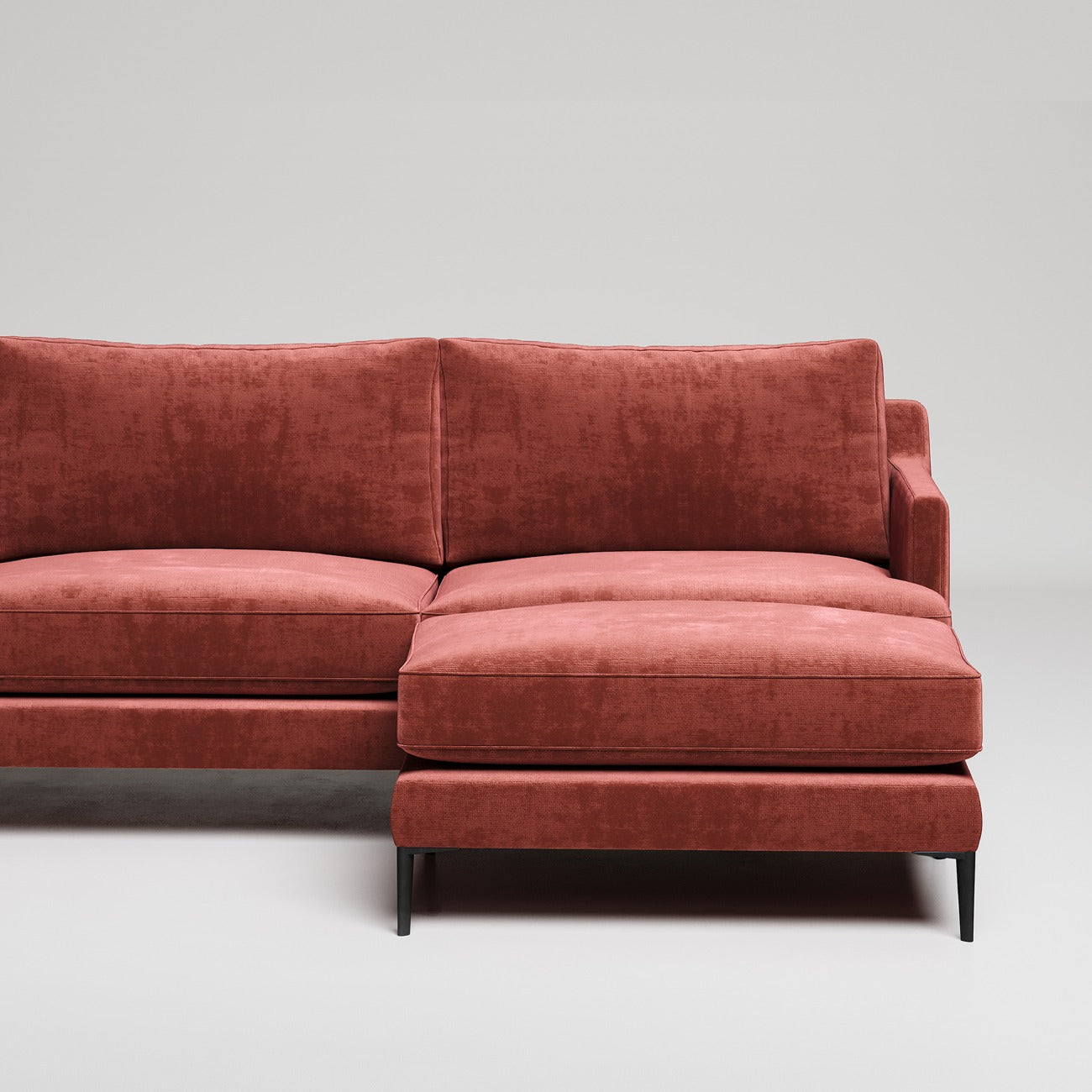 Modern L-shaped sectional sofa in rust velvet upholstery with black metal legs against white background