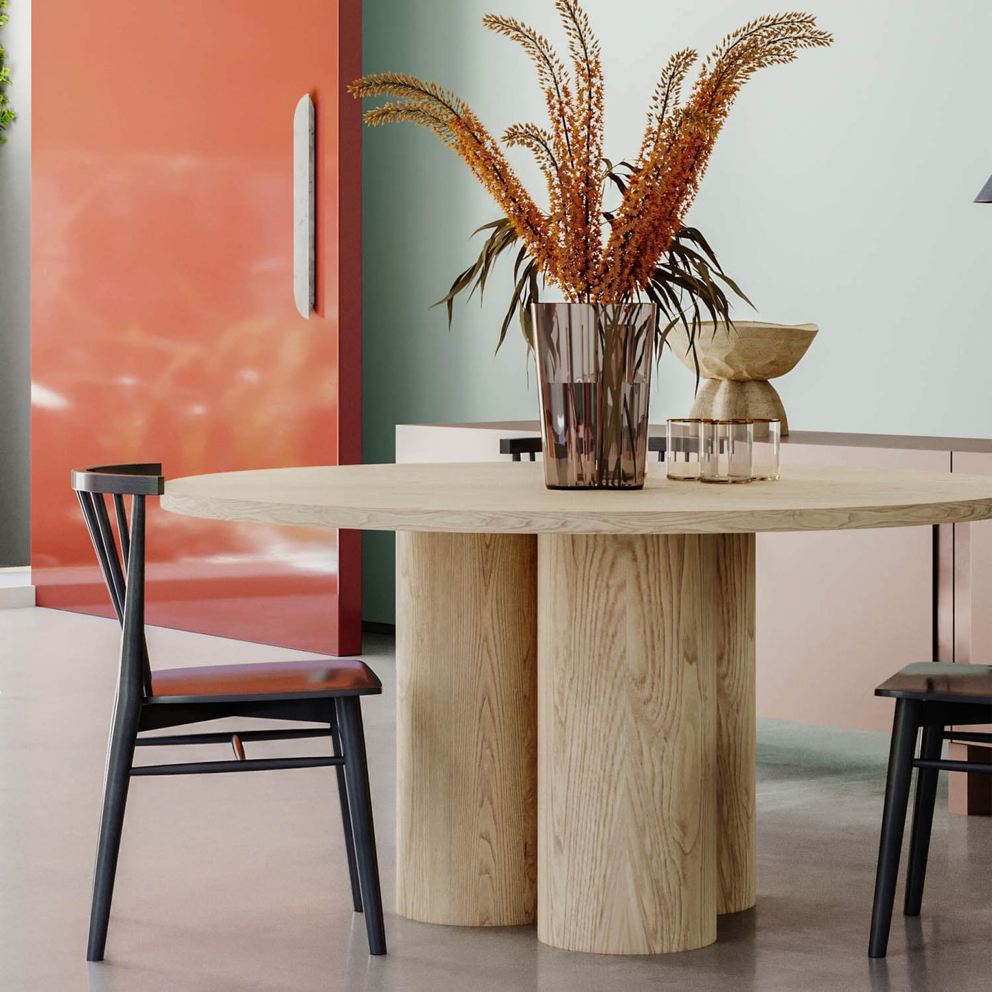 Modern dining room with round wooden table, black chairs, coral wall, and dried pampas grass centerpiece