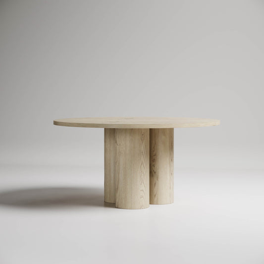 Modern round dining table with light wood finish and sculptural cylindrical base legs against neutral background