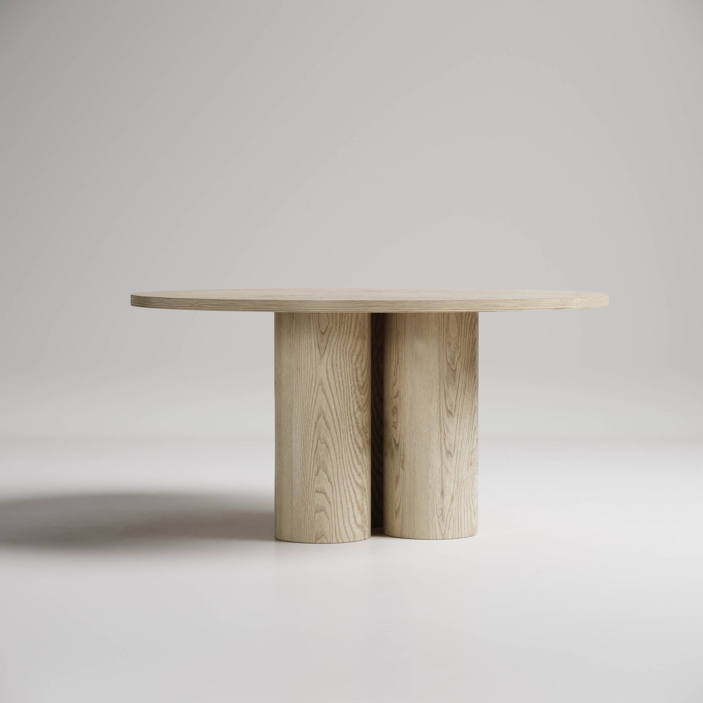 Modern round dining table with twin cylindrical pedestal base in light wood, minimalist design against gray background