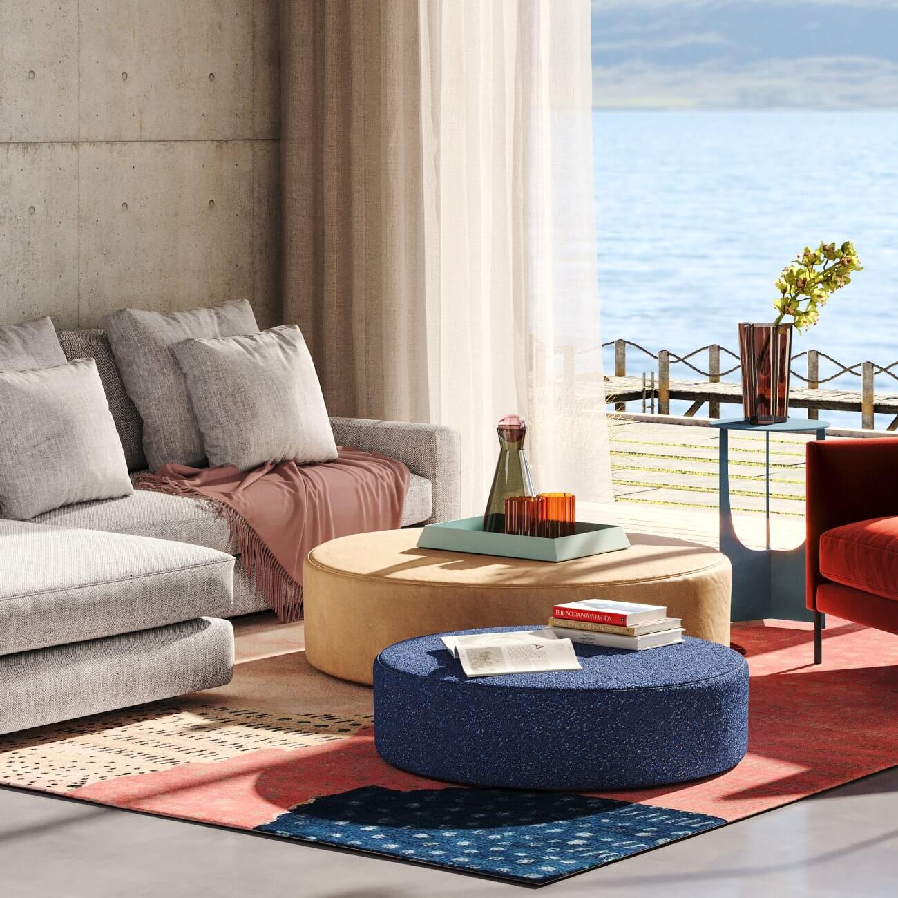 Modern coastal living room with gray sofa, round ottomans, ocean view, and coral accent rug