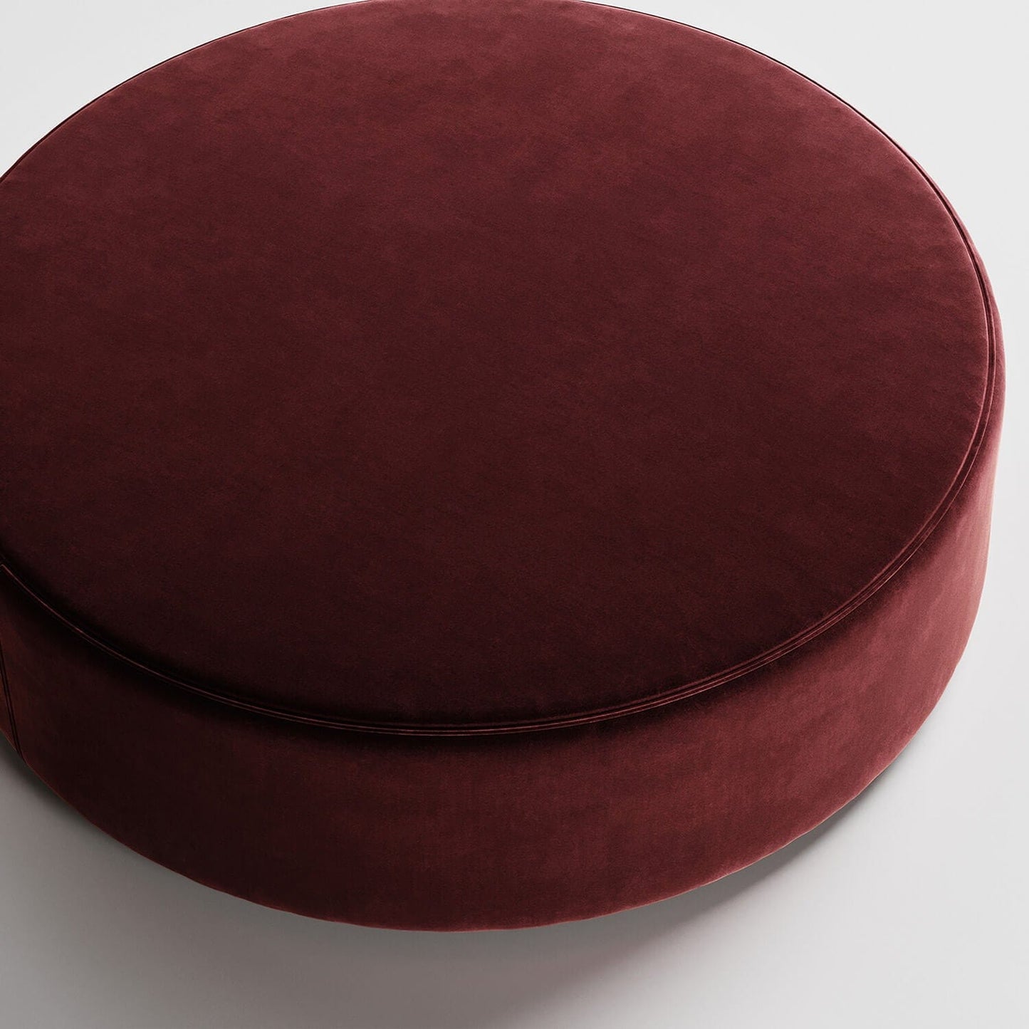 Round burgundy velvet ottoman or pouf against white background, viewed from above