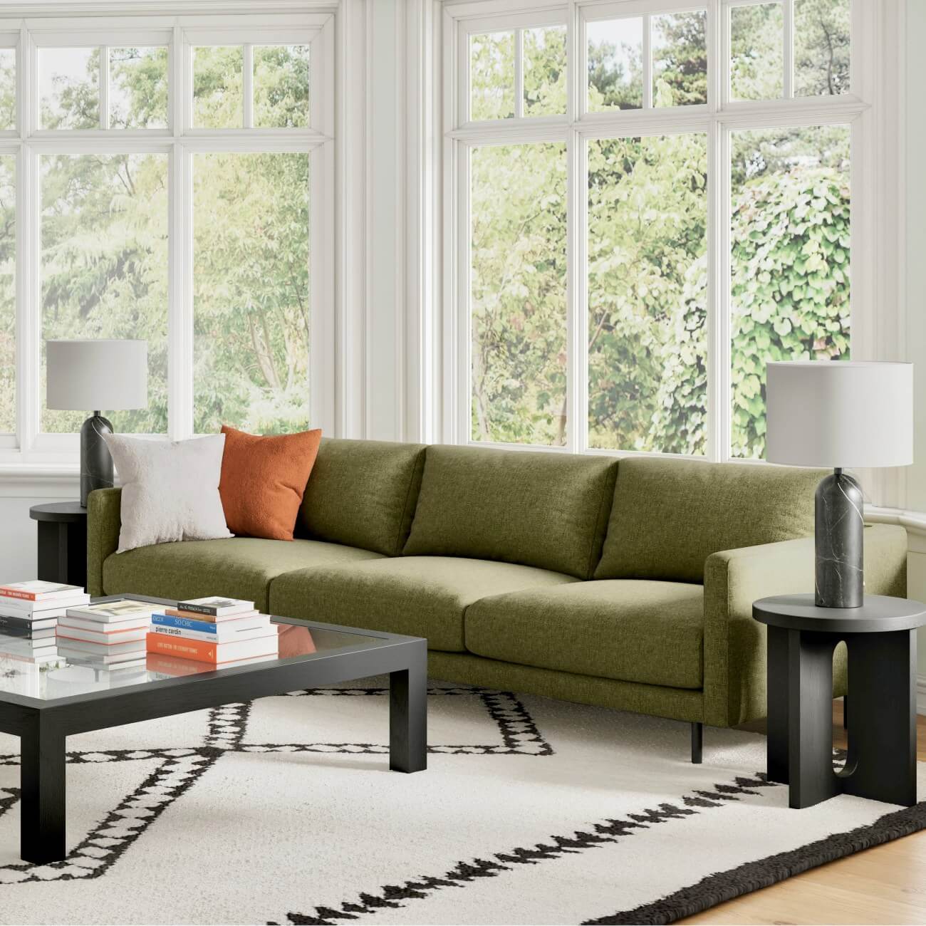 Modern living room with olive green sofa, black accent tables, geometric rug, white windows overlooking greenery