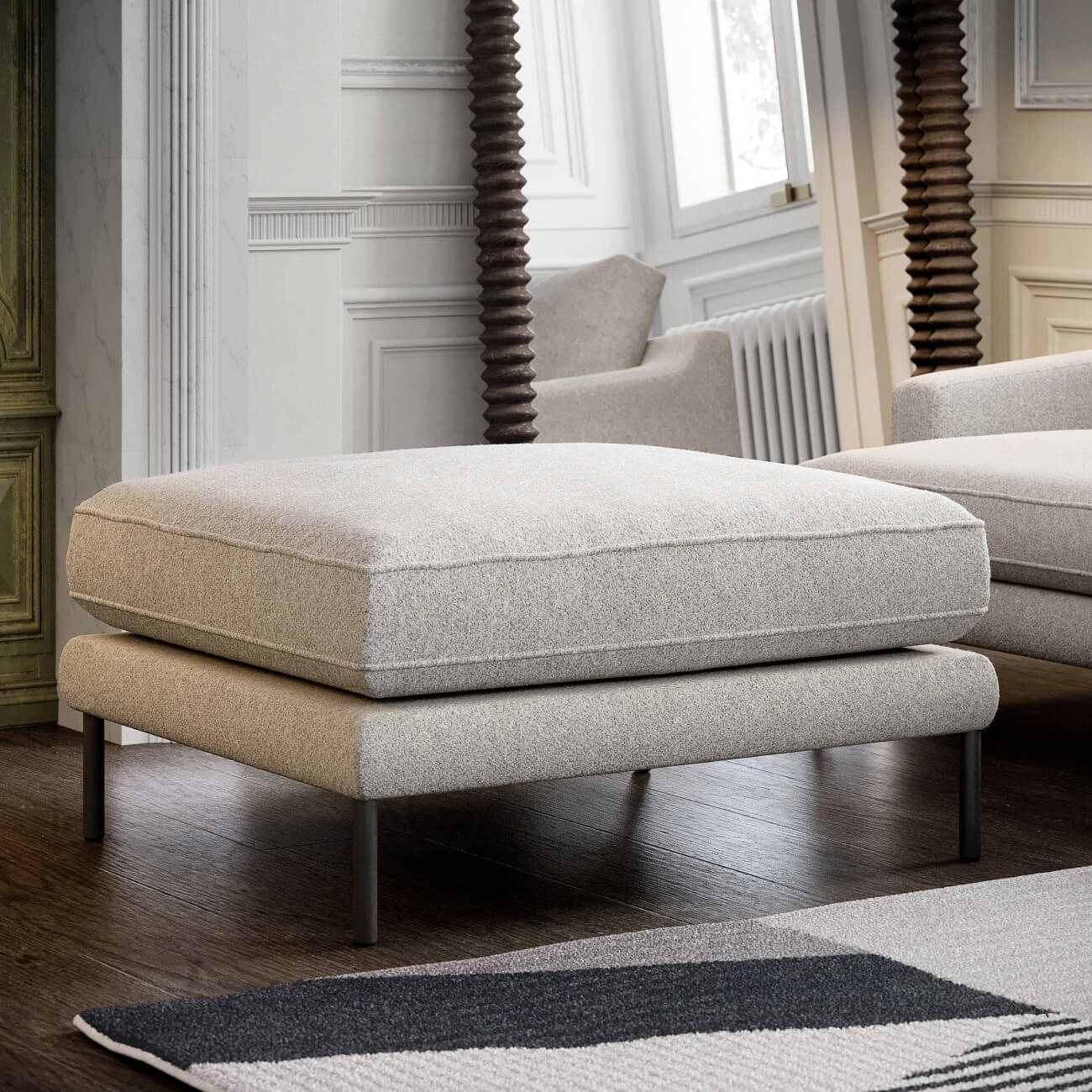 Modern grey upholstered ottoman on metal legs with spiral wood posts and white wainscoting in background