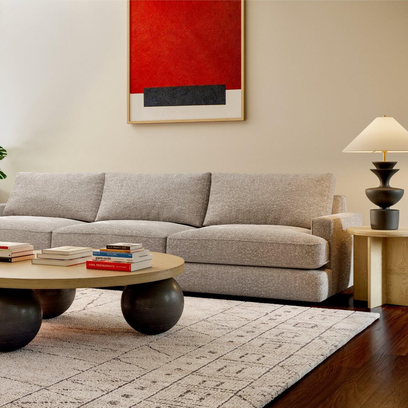 Modern living room with grey sectional, round wood coffee table, abstract red art, geometric rug, statement lamp
