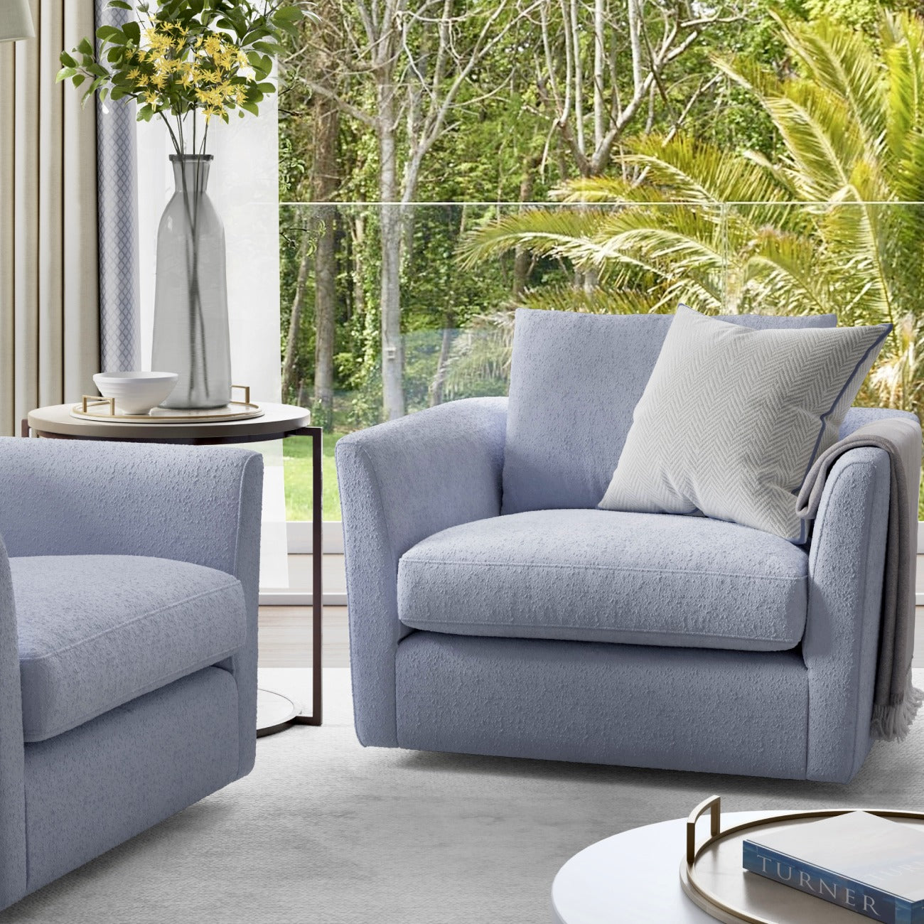 Modern gray swivel armchairs with throw pillows, side table with vase, tropical garden view through window