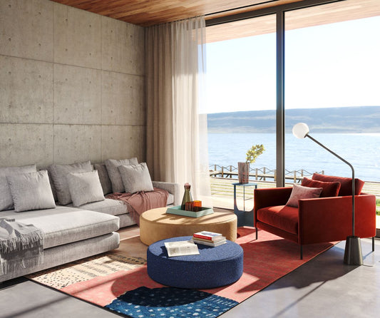 Modern coastal living room with concrete walls, gray sofa, red chair and ocean view through floor-to-ceiling windows